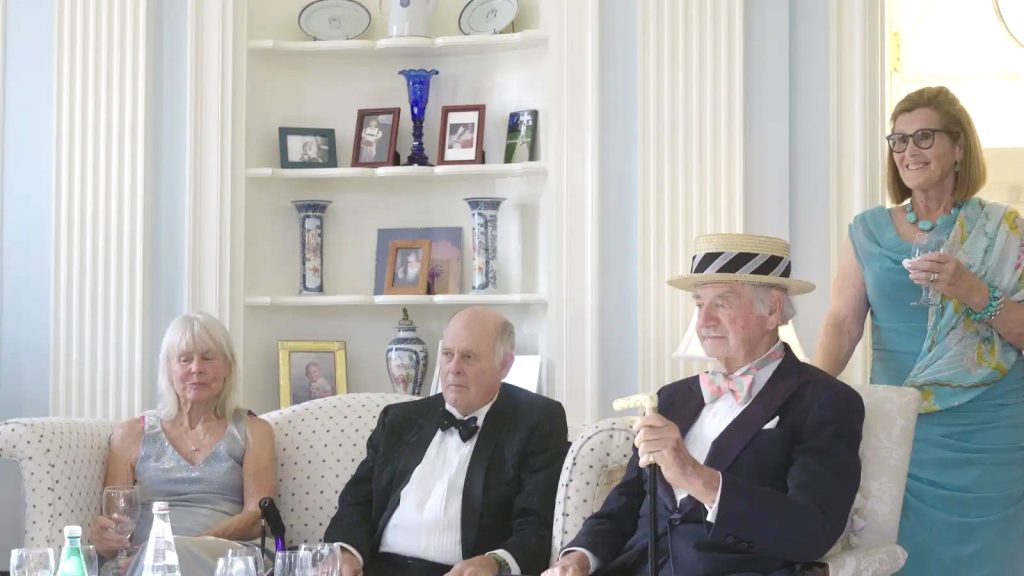 Mr. Fleming, seated in a straw hat, and guests gathered in the sitting room for the Summer Solstice Musicale.